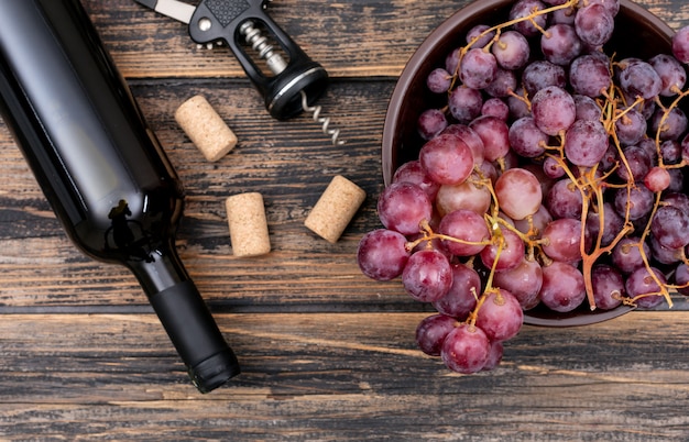 Foto gratuita bottiglia di vino di vista superiore con l'uva in ciotola sull'orizzontale di legno scuro