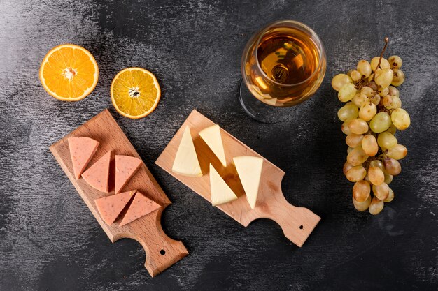 Top view of wine glass and cheese on wooden cutting board on dark  horizontal