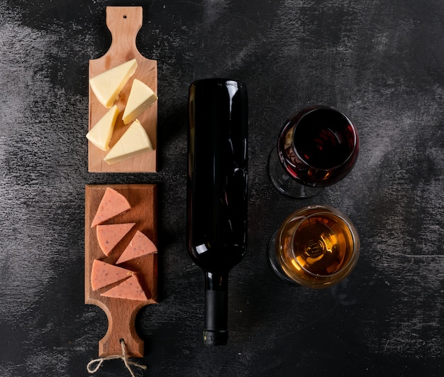 Top view of wine glasses and cheese on wooden cutting board on dark  horizontal