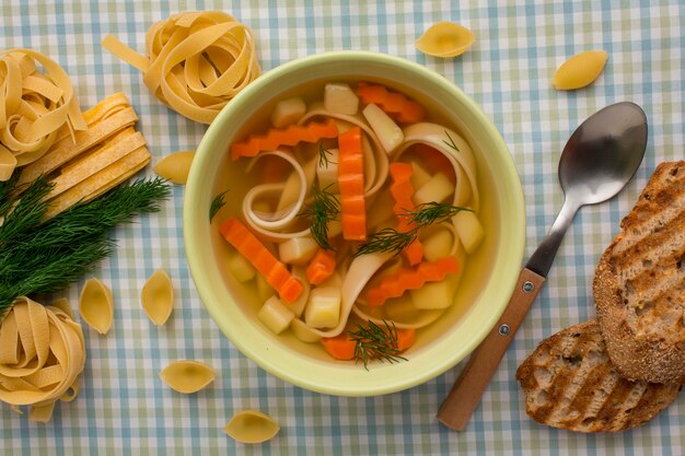 Top view of winter vegetables soup in bowl with spoon and tagliatelle