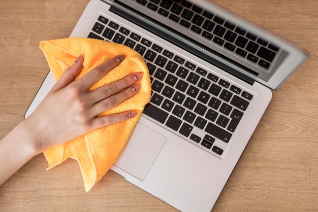 Top view of woman cleaning laptop with cloth