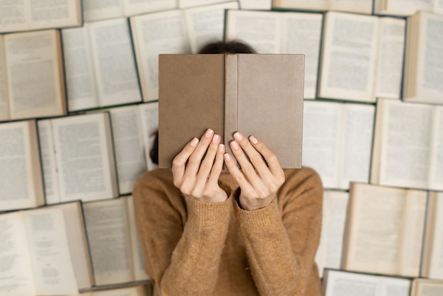 Верхний вид женщина в уютном мягком свитере лежит на открытых книгах