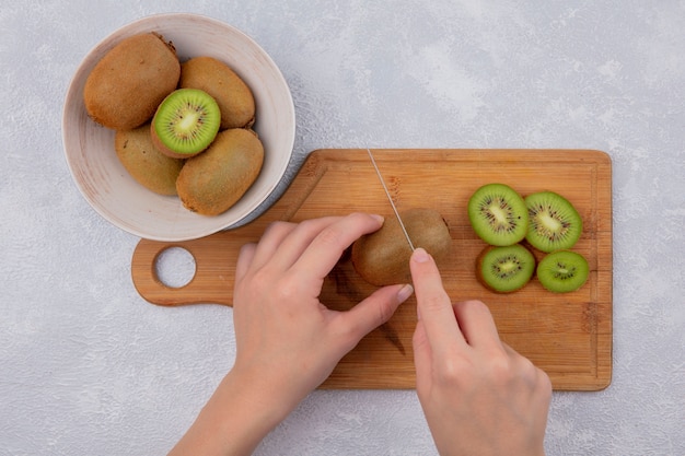Top view  woman cuts kiwi on cutting board and in bowl on white background