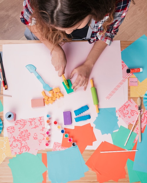 Top view of woman cutting colorful clay on paper