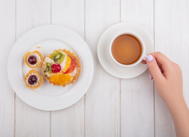 Top view  woman drinking cup of tea with tartlets on plate on white background