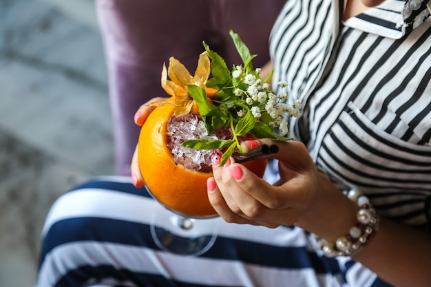 Top view woman drinks refreshing cocktail in orange with flowers in the form of decor