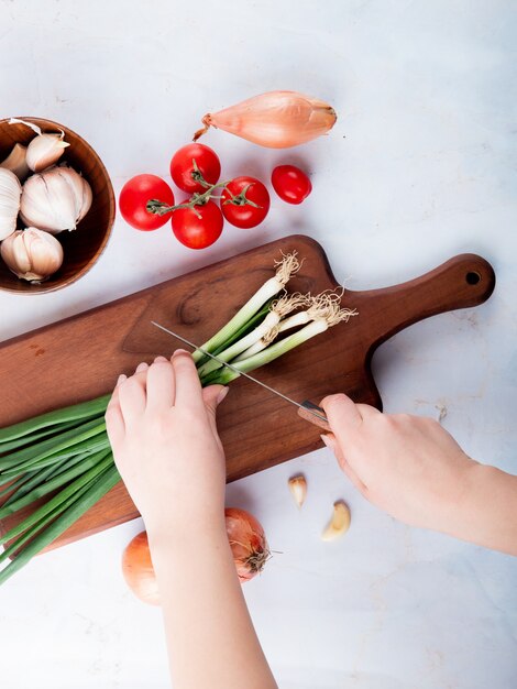 Top view of woman hand cutting onion on cutting board with tomato garlic on white background