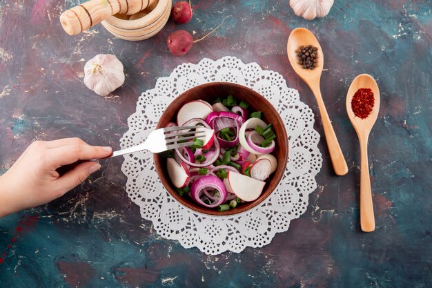 Top view of woman hand eating vegetable salad with radish onion and scallion on green and maroon background
