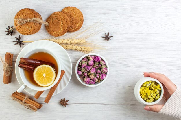 Top view of woman hand holding herbal in a pot with black tea with cinnamon lime lemon and various herbals cookies on white background