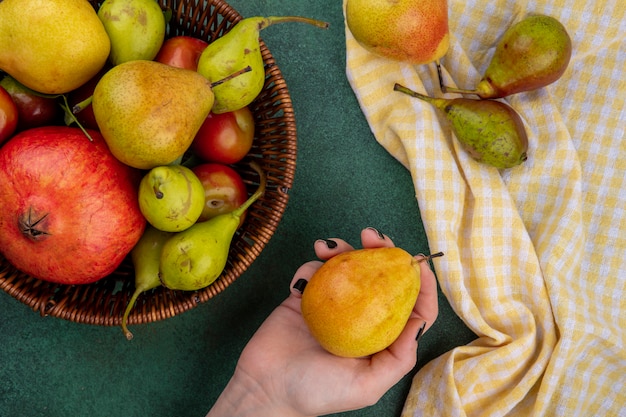 Free photo top view of woman hand holding peach with basket of pomegranate peach plum on green surface