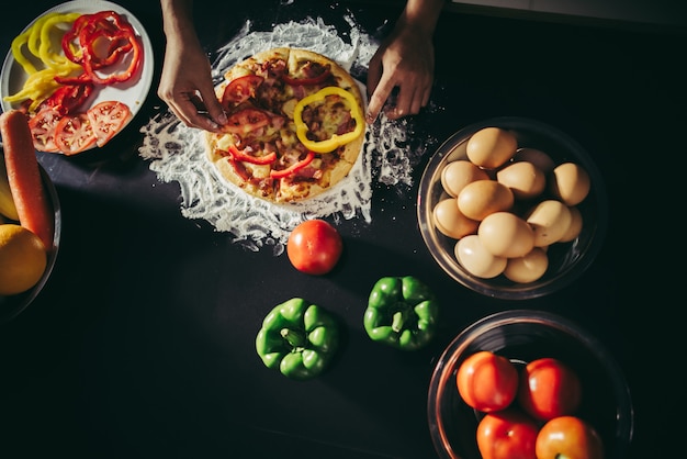 Top view of woman hand put topping on homemade pizza.