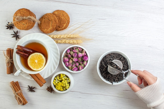 Top view of woman hand taking dry tea black tea with cinnamon lime lemon and various herbals cookies on white background