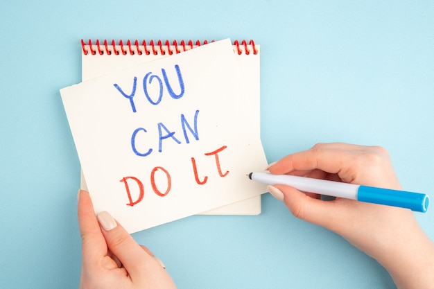 Top view woman hand writing you can do it on sticky note on blue