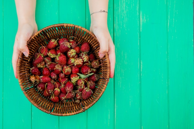 Top view of woman hands holding basket with strawberries on left side and green table