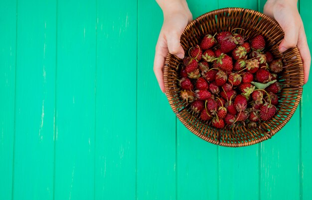 Top view of woman hands holding basket with strawberries on right side and green table