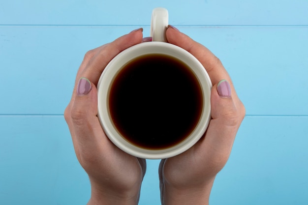 Top view of woman hands holding cup of tea on blue background