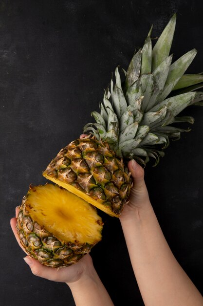 Top view of woman hands holding cut pineapple on black surface