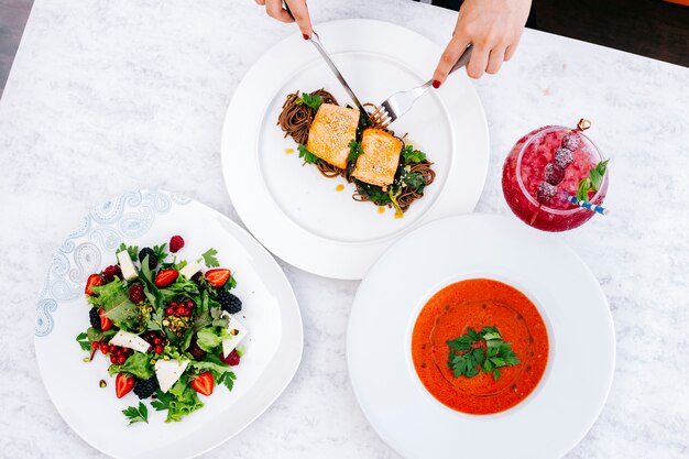 Top view of woman having lunch with salmon with brown noodles soup, berry salad and cocktail