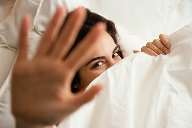 Top view of woman hiding under the sheets at home