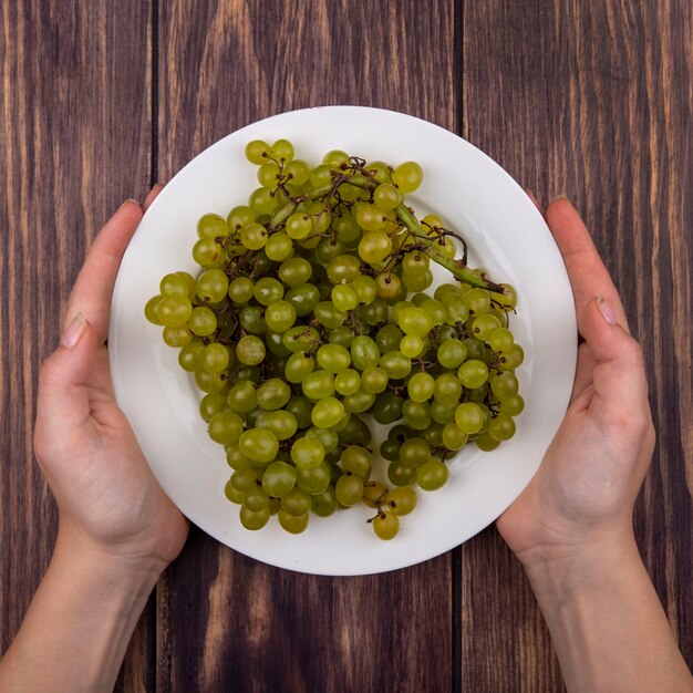 Top view woman holding green grapes on a plate on wooden wall