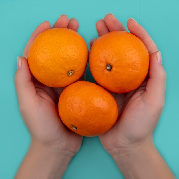 Top view  woman holding oranges in her hands on a turquoise background