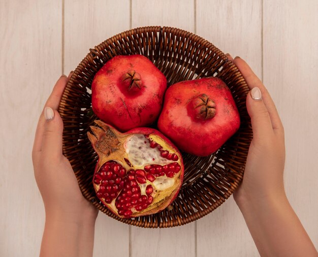 Top view woman holding pomegranates in a basket on a white wall