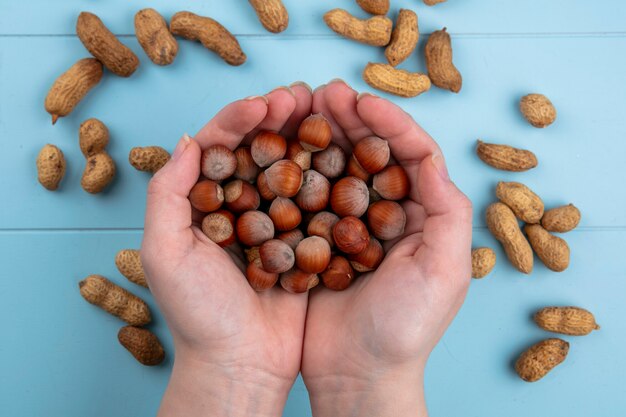 Free photo top view woman holds in her hands walnuts with hazelnuts and peanuts on a blue table