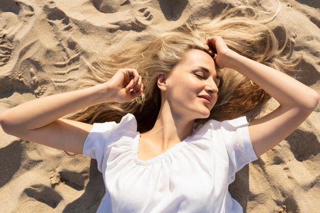 Vista superiore della donna che posa sulla sabbia della spiaggia