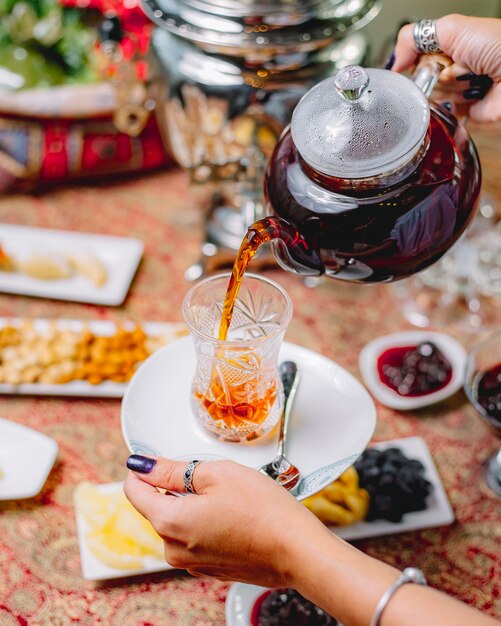 Top view a woman pours tea from a teapot into a glass of armuda on a saucer