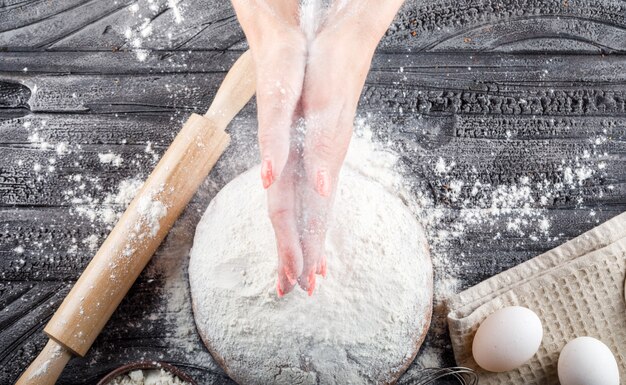 Top view woman preparing cake with rolling pin, flour, eggs on table on wooden surface. horizontal