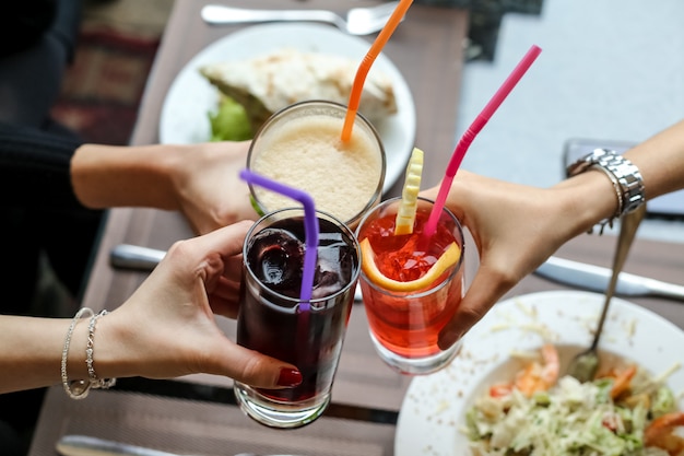 Free photo top view women drinking soft drinks cola fresh orange juice and lemonade with colorful straws