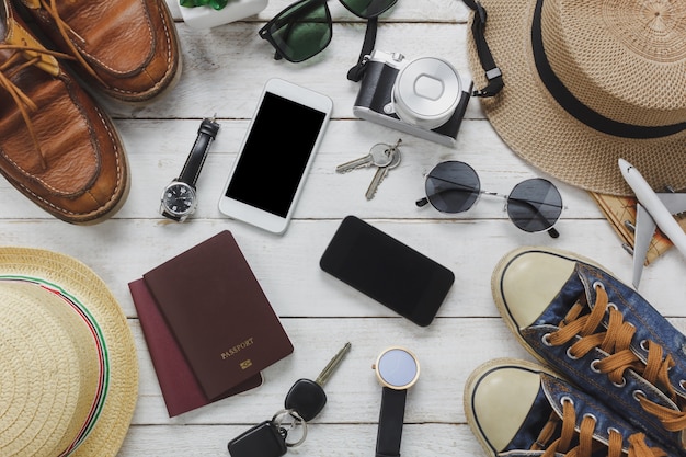 Top view women and man accessoires to travel concept.White and black mobile phone,airplane,hat,passport,watch,sunglasses,shoes and key on wood table.