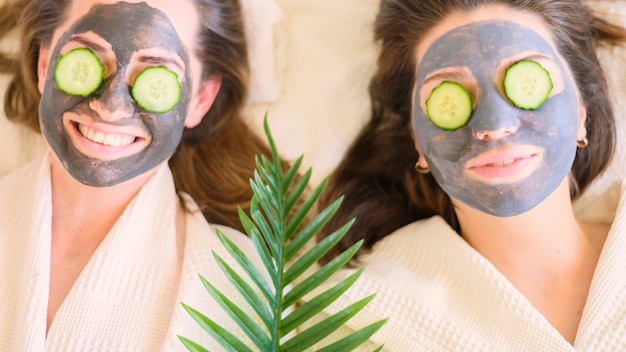 Top view of women with face masks and cucumber slices on their eyes