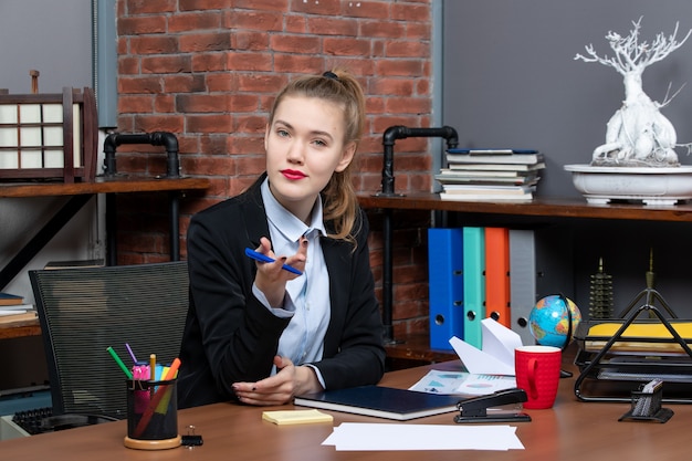 Free photo top view of wondering confident female office worker sitting at her desk and posing for camera