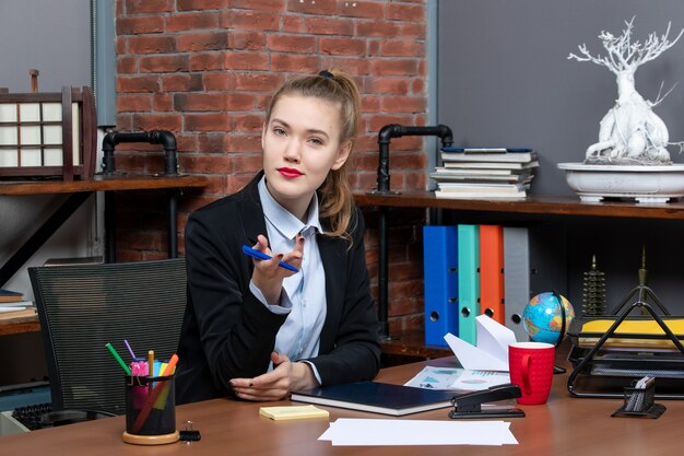 Top view of wondering confident female office worker sitting at her desk and posing for camera