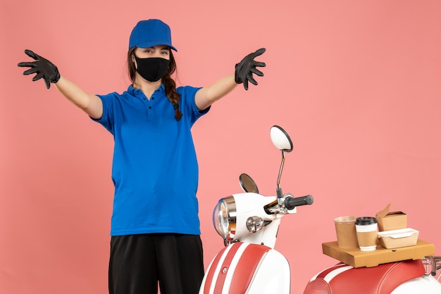 パステル ピーチ色のコーヒー ケーキとオートバイの隣に立っている医療マスク手袋を着て不思議な宅配便の女の子のトップ ビュー