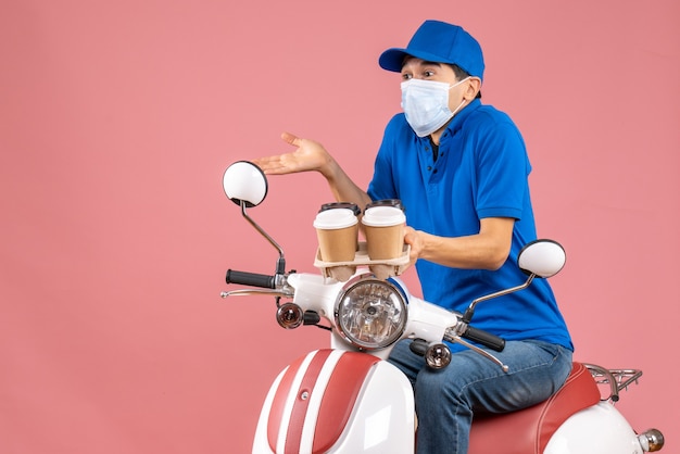 Vista dall'alto del corriere chiedendosi in maschera con cappello seduto su uno scooter che mostra ordini su pesca pastello on