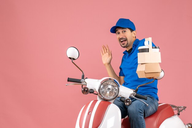 Top view of wondering courier man wearing hat sitting on scooter giving orders on pastel peach