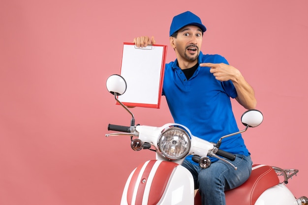 Top view of wondering courier man wearing hat sitting on scooter holding document on pastel peach