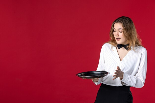 Foto gratuita vista dall'alto di chiedersi il papillon femminile del server sul collo e tenere il vassoio sul muro rosso