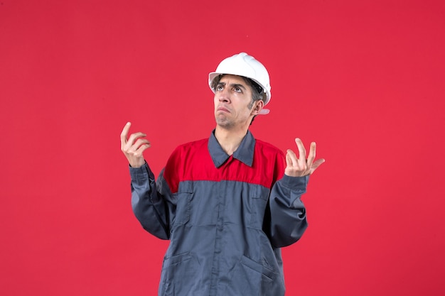 Вид сверху удивленного молодого строителя в униформе в каске на изолированной красной стене
