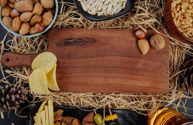 Top view of a wood board with nuts and beer snacks on straw 