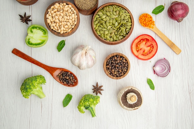 Top view wooden bowls with pumpkin seeds beans black pepper broccoli garlic wooden spoons cinnamons on table