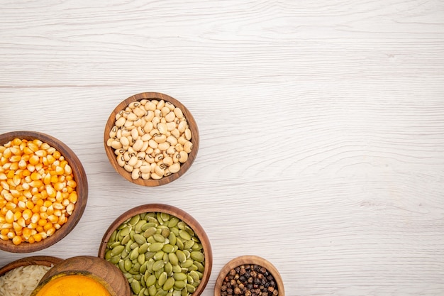 Free photo top view wooden bowls with pumpkin seeds black pepper beans on grey table