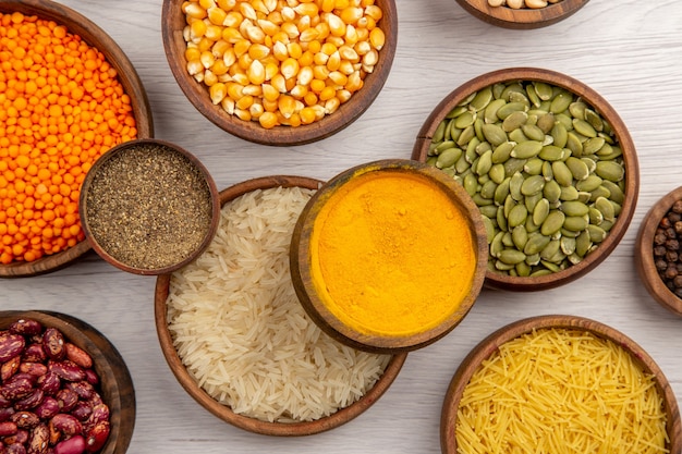 Top view wooden bowls with rice corn seeds pumpkin seeds beans lentiles thin pasta different spices on grey background