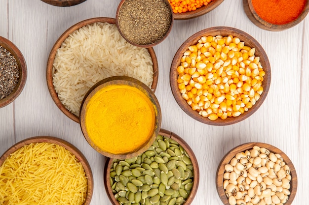 Top view wooden bowls with rice lentile pumpkin seeds black pepper turmeric beans thin pasta on grey table