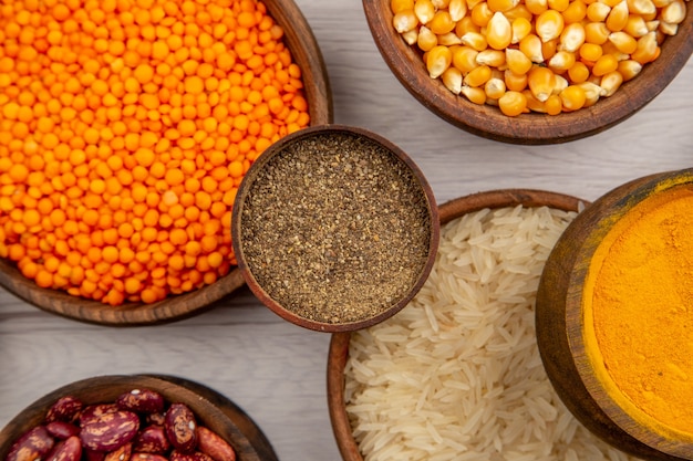 Top view wooden bowls with rice pumpkin seeds black pepper powder turmeric lentiles on grey background