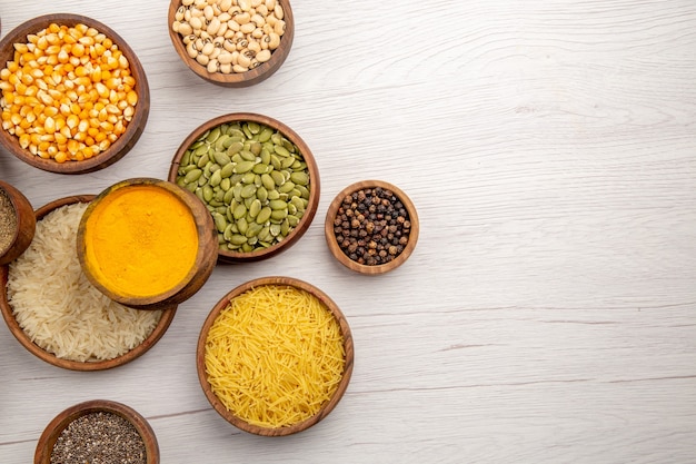 Top view wooden bowls with rice pumpkin seeds black pepper turmeric beans on grey table