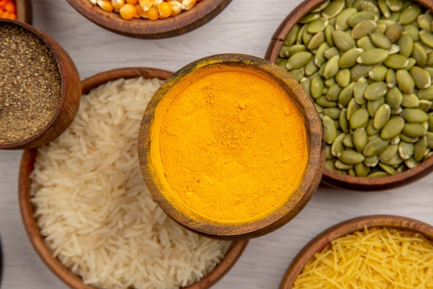 Free photo top view wooden bowls with rice pumpkin seeds thin pasta black pepper powder turmeric on grey background