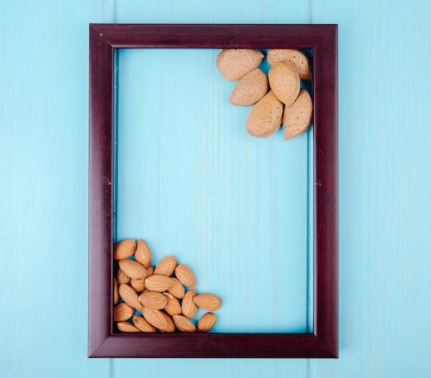 Top view of wooden empty picture frame with almond on blue wooden background